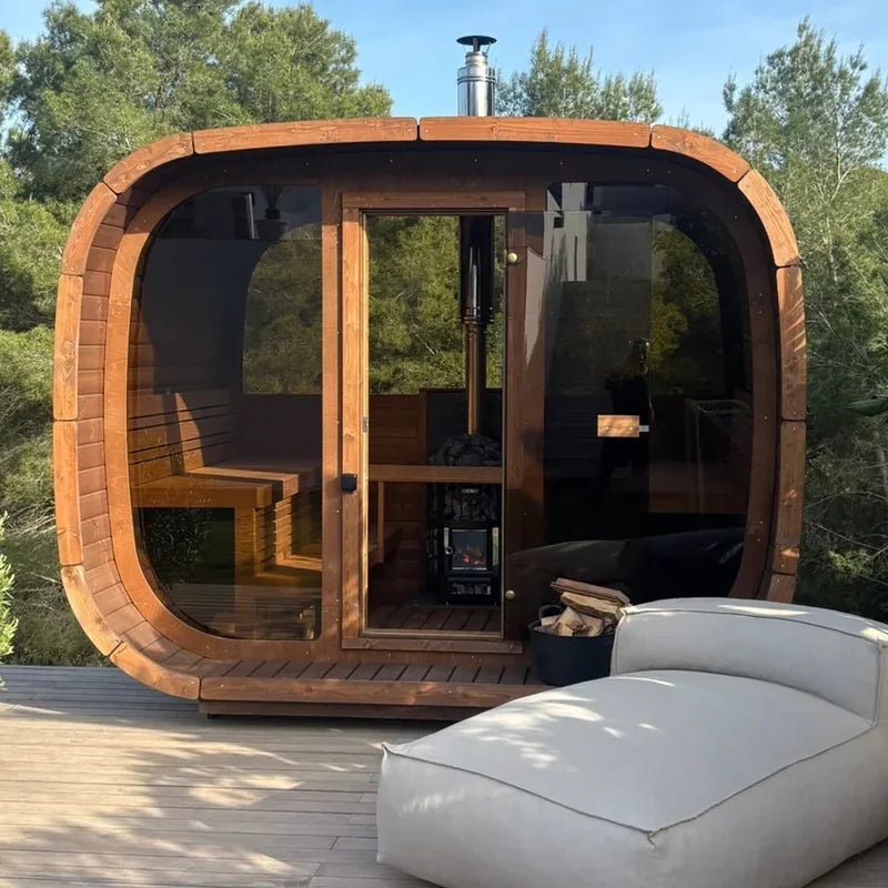ICON 300 Kube i termotre på en terrasse, sett rett forfra med helglassfront, glassdør og vedfyrt ovn med pipe