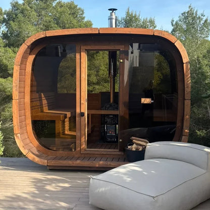 ICON 300 Kube i termotre på en terrasse, sett rett forfra med helglassfront, glassdør og vedfyrt ovn med pipe