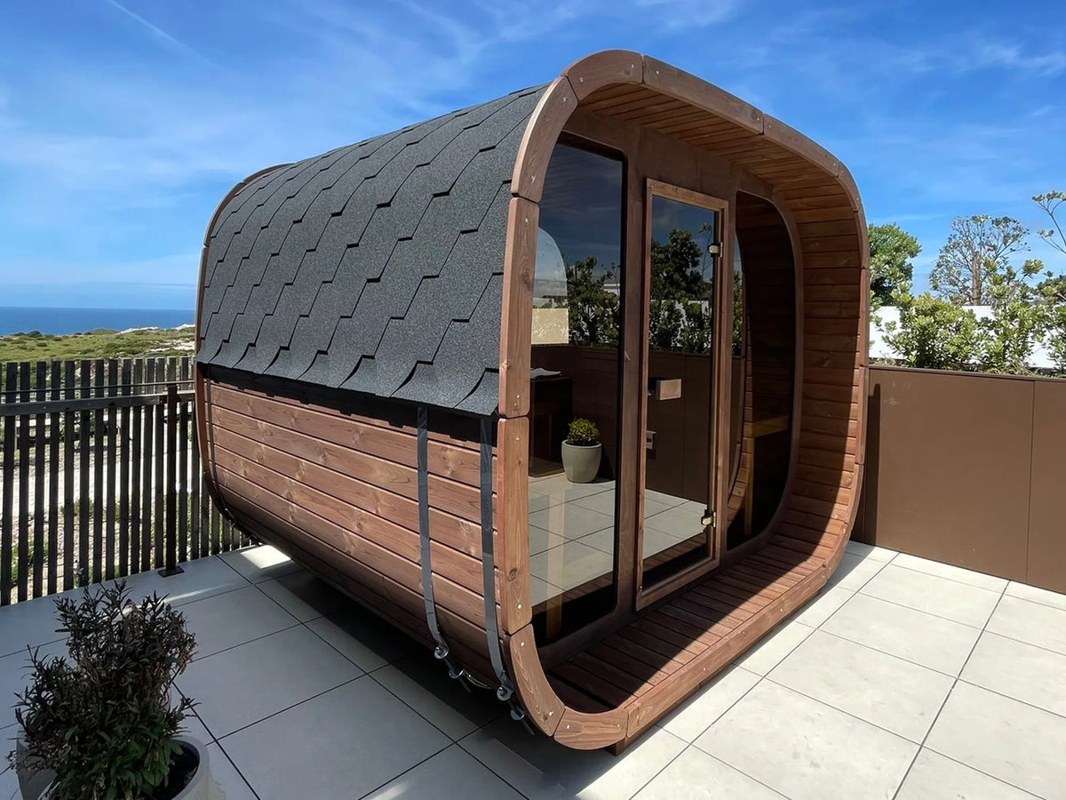 ICON 300 Kube sett skrått fra siden på en terrasse ved havet, med svart takshingel, rustfrie stålbånd og glassfront