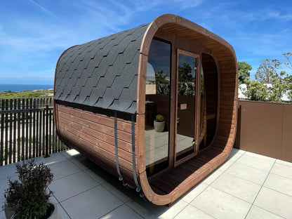 ICON 300 Kube sett skrått fra siden på en terrasse ved havet, med svart takshingel, rustfrie stålbånd og glassfront
